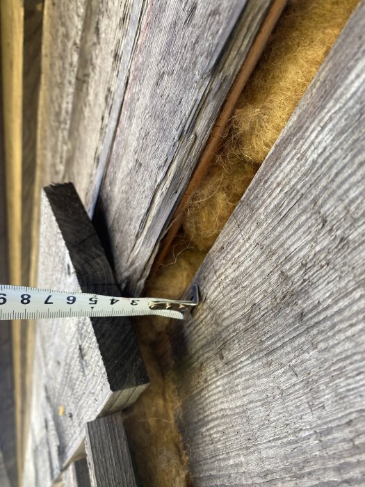 Mätband visar 4 cm glipa mellan trästockar på nybyggt timmerhus, med isolering synlig i sprickan.