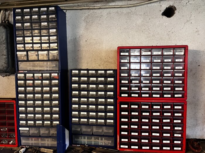 Sortimentslådor med plastfack märkta med etiketter. Lådorna är fyllda med olika smådelar för mekaniskt arbete, arrangerade mot en betongvägg.