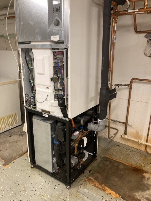 Ny värmepump installerad i källare, oinkopplad med kopparrör synliga. Står på ett betonggolv, redo för rörmokarens installation.