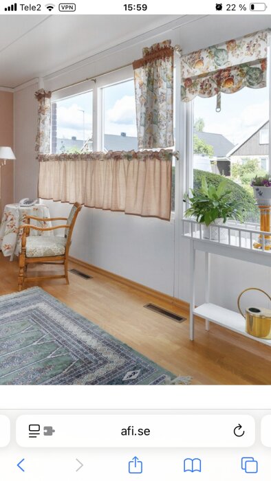 Interiör av ett rum i ett hus med ljusa gardiner, matta på golvet och tilluftsdon i golvet, uppvärmt av någon form av elpanna.