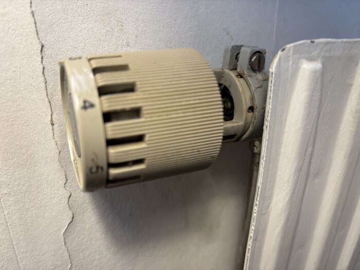 AGA-ventil på radiator med inställningsskala synlig, monterad mot en vägg med spricka i putsen.