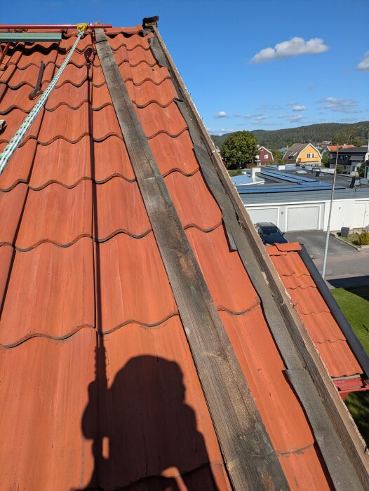 Rött tegeltak med vindskiva borttagen för målning, rep och säkerhetsutrustning synliga, solig dag med utsikt över grannskapet.