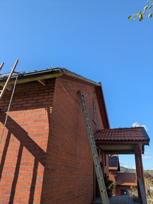 Röd tegelbyggnad med stege lutad mot vindskivan för målningsarbete. Knoxräcke och fallskyddssele används för säkerhet.