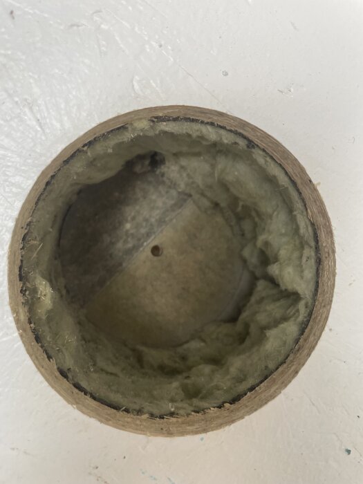 Hål i förrådspanel med synlig isolering och en skiva, fotograferat genom hålsågning och luftintag, ca 1 cm tjock.