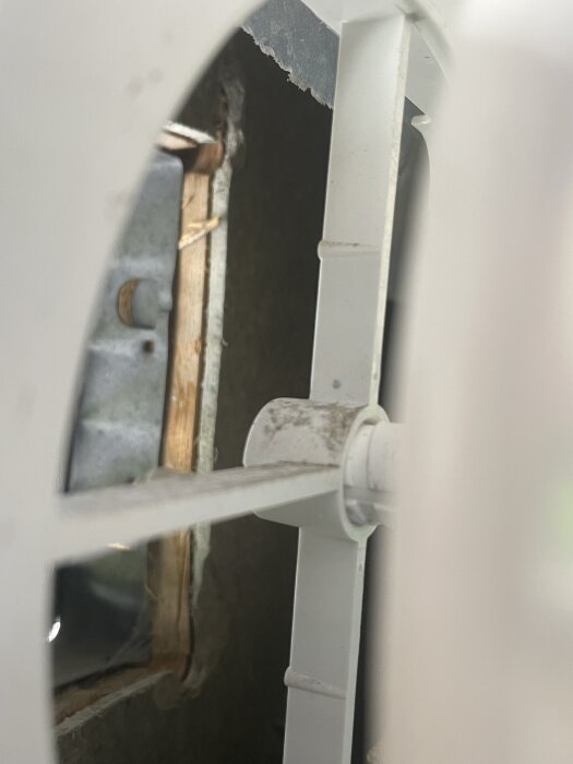 Inifrån syns en okänd platta genom ett hål i förrådspanelen, uppmålad bredvid ventilationsintag. Plattan verkar vara knappt 1 cm tjock.