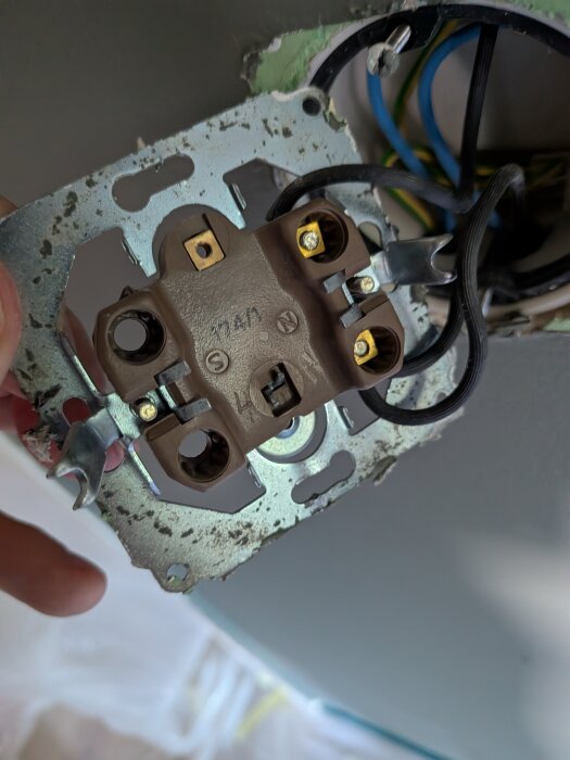 Gammal strömbrytare med flera skruvanslutningar, potentiellt en hotellbrytare, visas urkopplad med synliga blå och gula kablar i bakgrunden.