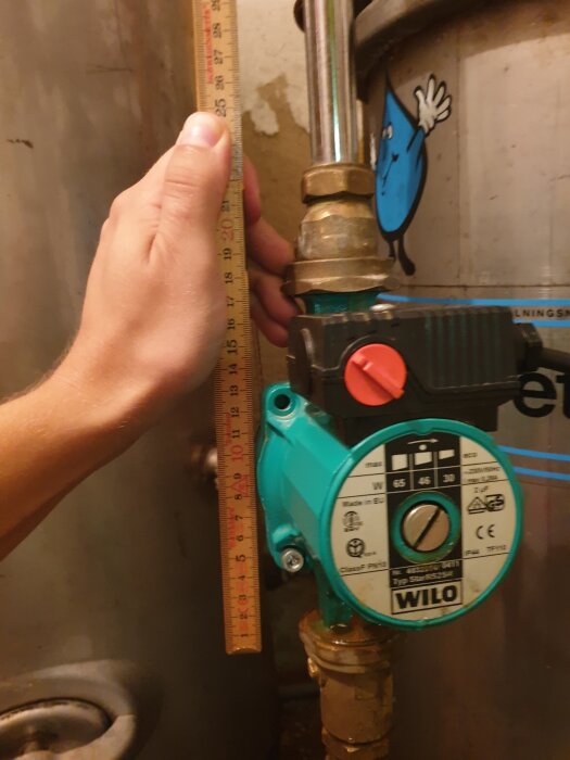 En grön Wilo StarRS 25/4 cirkulationspump med en linjal som mäter rörlängd monterad på ett vattenfilter.