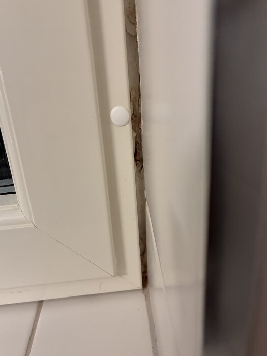 Fult fönsterhörn i renoverat badrum, där gångjärn tidigare satt; oavslutat arbete med synlig skada och mellanrum vid kakel och fönster.
