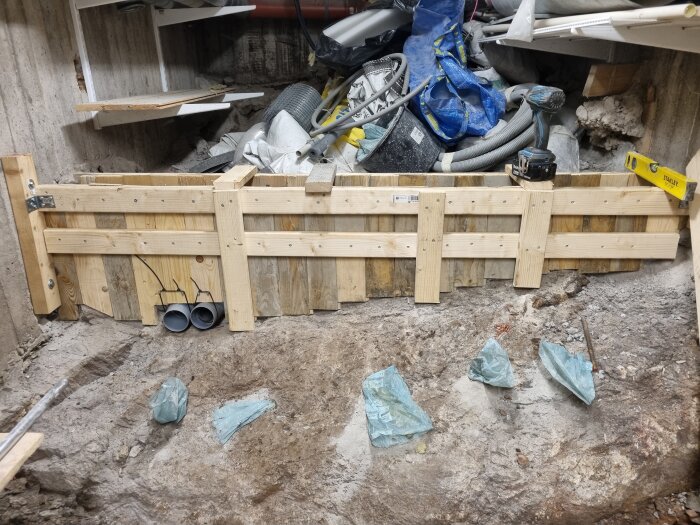 Hemmagjord gjutform framför en ojämn bergsyta i en byggmiljö, med verktyg och material liggande ovanpå.