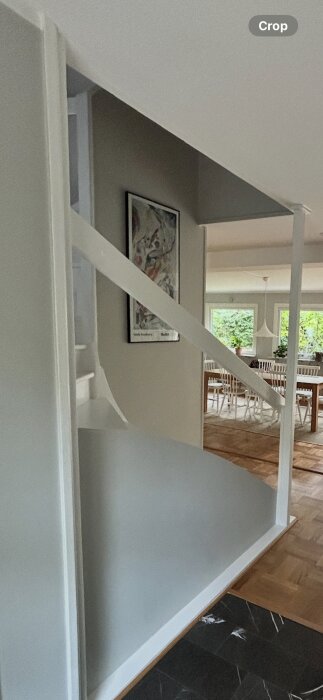 Öppen passage med vita väggar och bjälke. Tavla på väggen och öppning till matbord med stolar i bakgrunden.