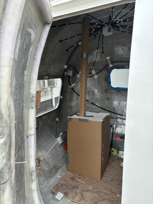 Wellpappmodell av bastuaggregat och skorsten placerad i en vagns interiör för att bestämma optimal position och balans inför monteringen.