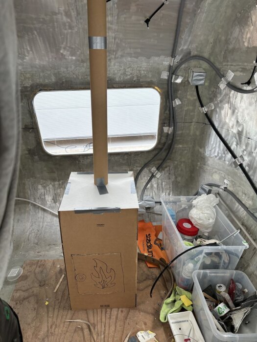 Prototyp av bastuaggregat av kartong med pappersrör som skorsten, omgiven av verktyg och material i en oisolerad vagn.