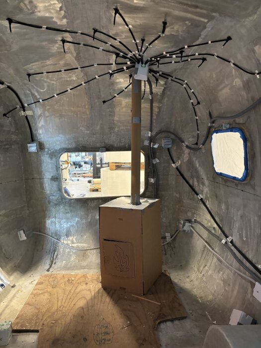 Modell av bastuaggregat i wellpapp placerad i vagnens interiör, med rör kopplade i taket och diverse ledningar synliga mot en metallvägg.