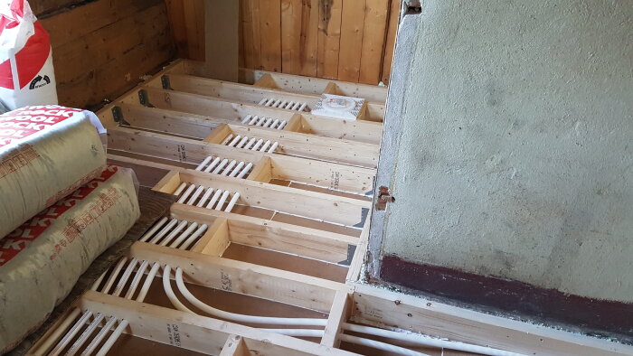 Golvreglar i ett badrum med vit slangdragning pågår, Rockwool-isolering syns i bakgrunden.