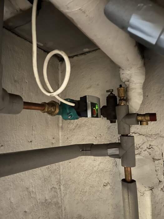 Rör och elektronisk komponent i ett pannrum; lampan lyser grönt.