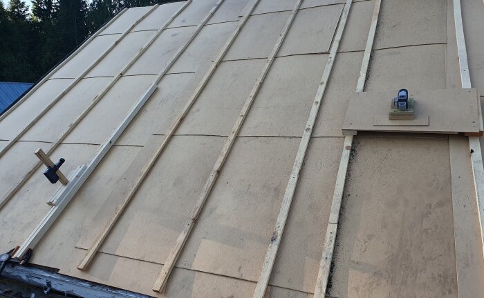 Tak med oljeboard och ströläkt monterad, förberett för ny plåttäckning, en laser används för att mäta takets planhet.