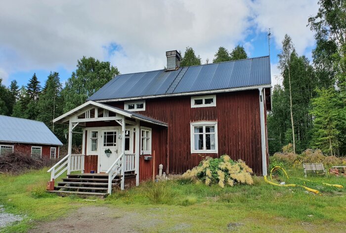 Rött hus med nymonterat plåttak, vit veranda och omgivande grönska, tydligt renoverat enligt beskriven process.