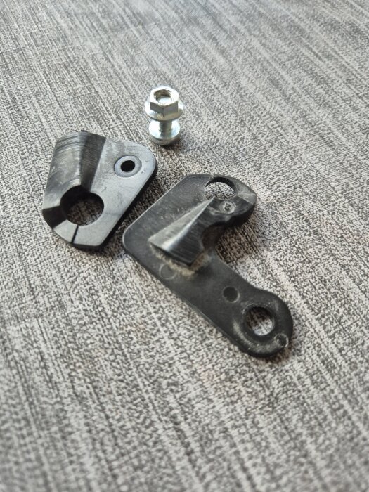 Plastbitar och en metallmutter på en grå yta, del av kylskåpsreparation för gångjärn vid dörr, ersätter trasiga plastdetaljer.