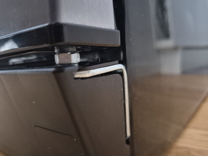 Närbild på kylskåpsgångjärn med hemmagjord lösning av metallmutter som ersätter plastdel för justering av dörrens öppning och stängning.