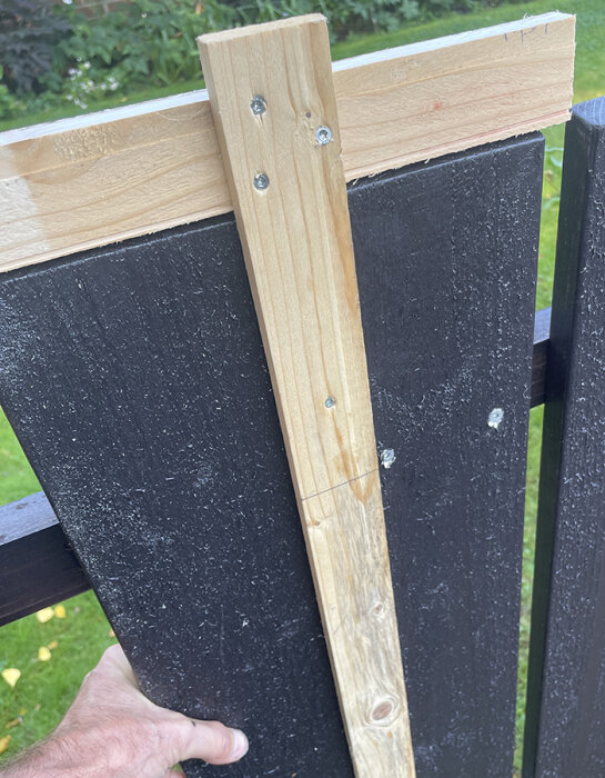 Trästaket med ny bräda och längdmall, fastsatt med skruv. Personen håller i mallen för att justera höjden på nästa bräda.