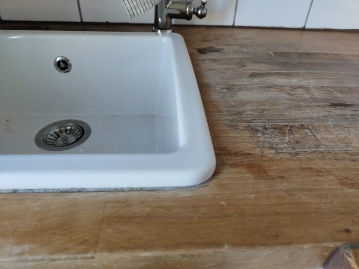 Sliten träbänk vid vit diskho med kaklad vägg i bakgrunden.