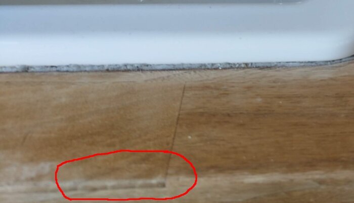 Närbild av en träyta med svullnad, eventuellt en lamellskiva. Ett område inringat i rött visar tydliga linjer i materialet.