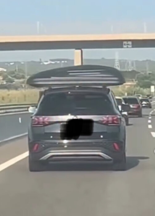 Bil med takbox kör på motorväg under en bro.