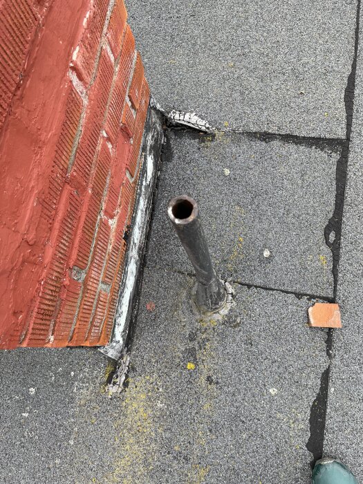Bild av rött tegelväggsmöte och tak, asfaltsklister synligt vid rör och sprickor. Potentiellt orsak till vattenskada.