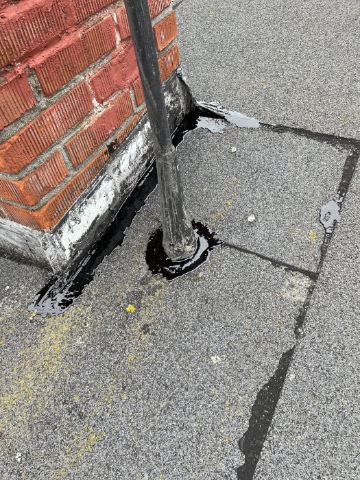 Rör på tak med svart asfaltsklister vid basen nära tegelvägg för att åtgärda möjlig vattenskada.