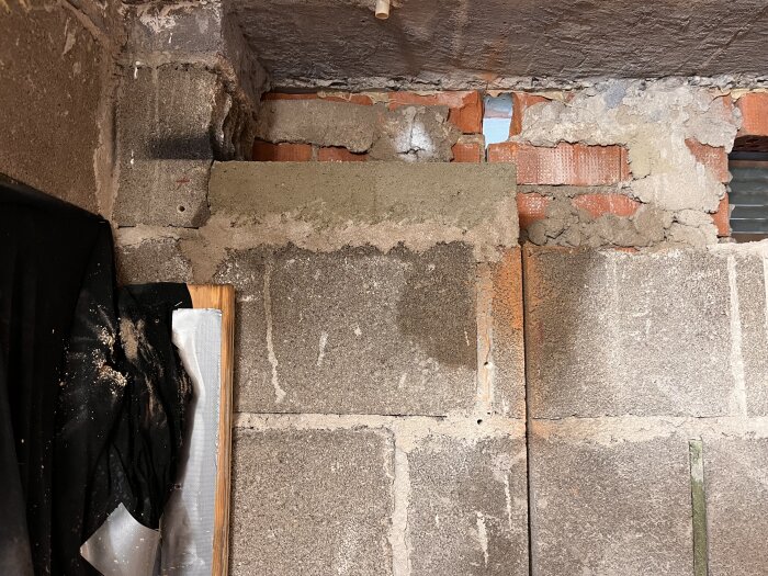 En murad vägg med betongklack syns, där en undergjutning för en balk planeras. Tegelsten och puts synliga, med ojämna fogar upptill.
