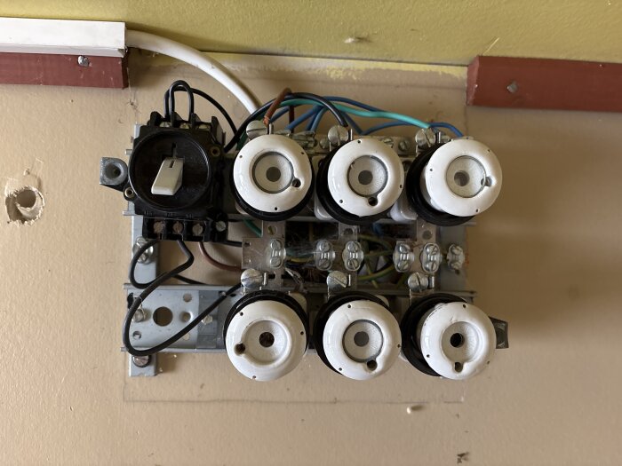 En elcentral med flera proppar och kablar monterad på en vägg, ser oprofessionellt installerad ut.