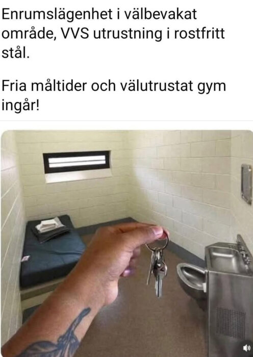 En hand med tatuering håller nycklar framför ett enkelt inrett rum med säng, fönster och kombinerad toalett och handfat i rostfritt stål.