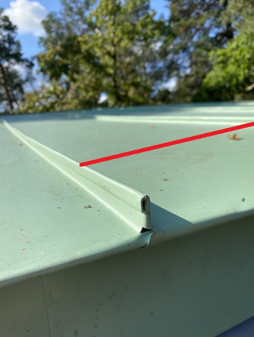 Metalltak med grön färg och en metallkant i närbild, skadad vid kanten. Röd linje för markerat område. Träd och himmel i bakgrunden.