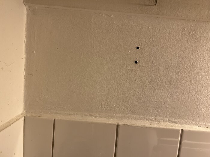 Två borrhål i en vägg ovanför vita köksplattor, där det vänstra hålet upplevs som stoppat av ett svart material.