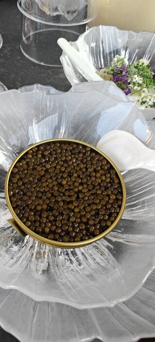 En burk kaviar i en glasskål med blommor runt omkring.