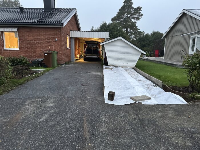 En uppfart vid ett tegelhus där markduk och kantsten nyligen har lagts ut på marken bredvid en bil.