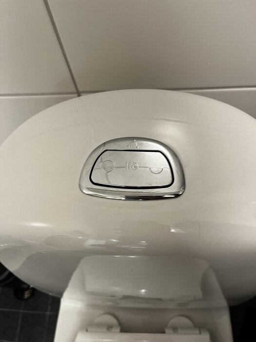 IFÖ WC-spolknapp på vit toalett med delad spolmekanism, sedd ovanifrån.