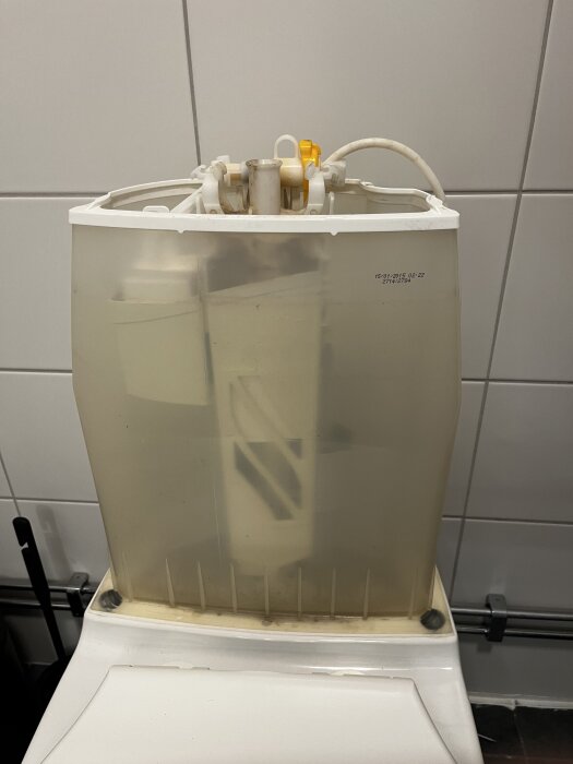 Öppen cistern på en IFÖ Toalett från 2015 med synliga rör och mekanism, möjligt problem med långsamt vattenflöde i tanken.