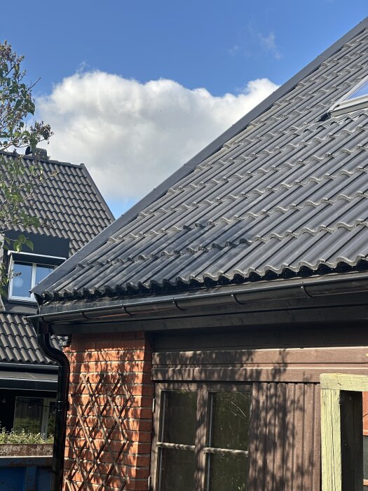 Nyinstallerat tak med svarta takpannor, hängränna och stuprör på tegelhus. Takpannorna verkar sluta högt på fotplåten.