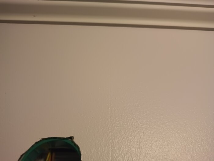 Vägg med slät ytstruktur målad med Timantti färg, genomgångshål i nederkanten, antydan till ojämnheter syns.