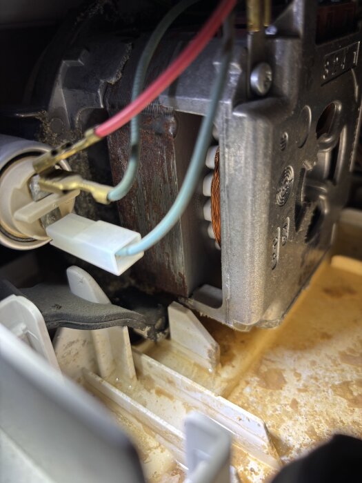 Diskmaskinens insida med en synlig motor, kalkavlagringar och vattenansamling, vilket antyder ett möjligt läckageproblem.