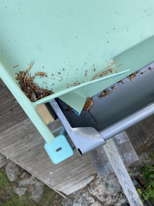 Vy från taket med smuts och barr i hängrännan, trätrallen synlig nedanför.