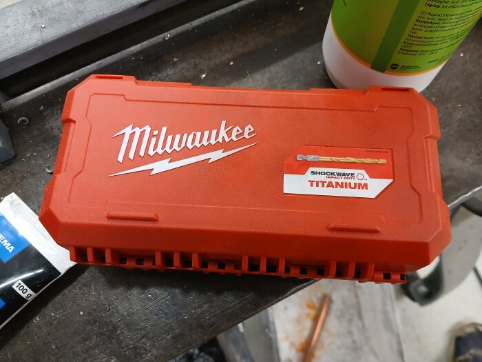Röd Milwaukee plastförpackning för borr, märkt "Shockwave Impact Duty Titanium", liggande på en verkstadsbänk.