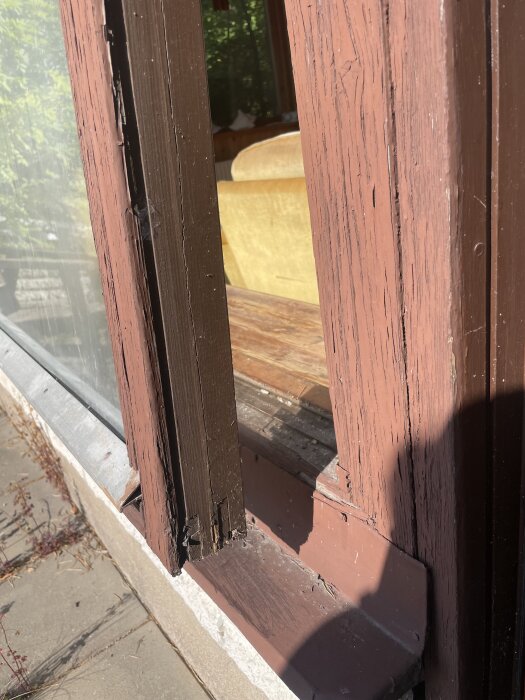 Ett gammalt fönster med mjölkig glasyta och sliten träkarm, visar solbelyst yta och skuggor utomhus.