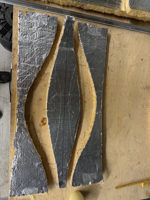 Delar av isolering skurna för att skapa en 90 graders böj med lamell, uppdelade i tre sektioner på en träyta.