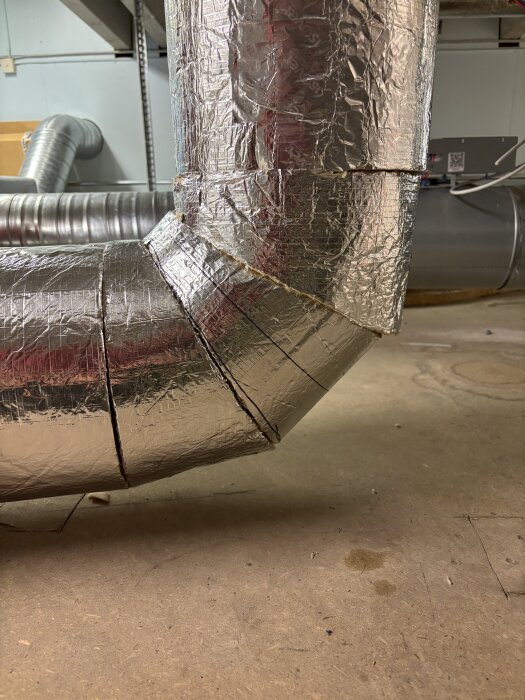 Isolerade ventilationstrummor med en 90-graders böj, delade i tre sektioner, visas på en verkstadsgolv.