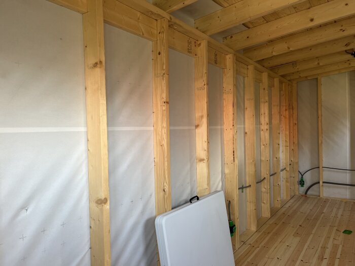 Inramad träramkonstruktion med isoleringsmaterial och synliga elledningar i en delvis isolerad friggebod. Golv av trä och insatt elskåp ses.