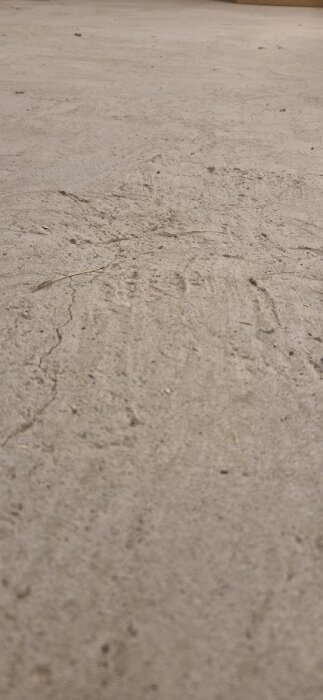 Ojämnt betonggolv med små sprickor och skrovlig yta i en tvättstuga.