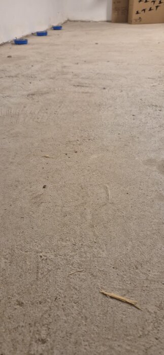 Rått ojämnt betonggolv i en tvättstuga, med små sprickor och ojämnheter, sett från en låg vinkel.