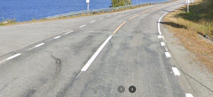 Asfaltväg vid sjön med en gul mittlinje i Norge, omgiven av räcken och grönska.